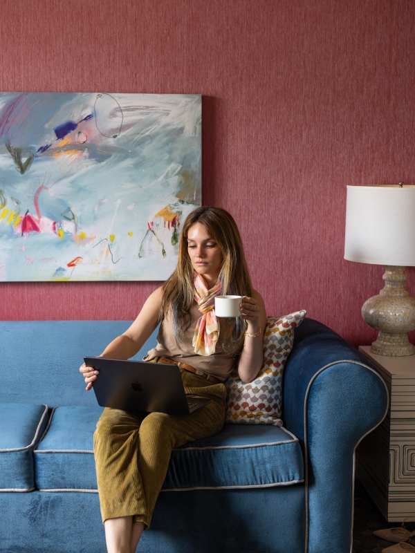 A woman looking at her laptop while holding a cup of coffee at The Marker