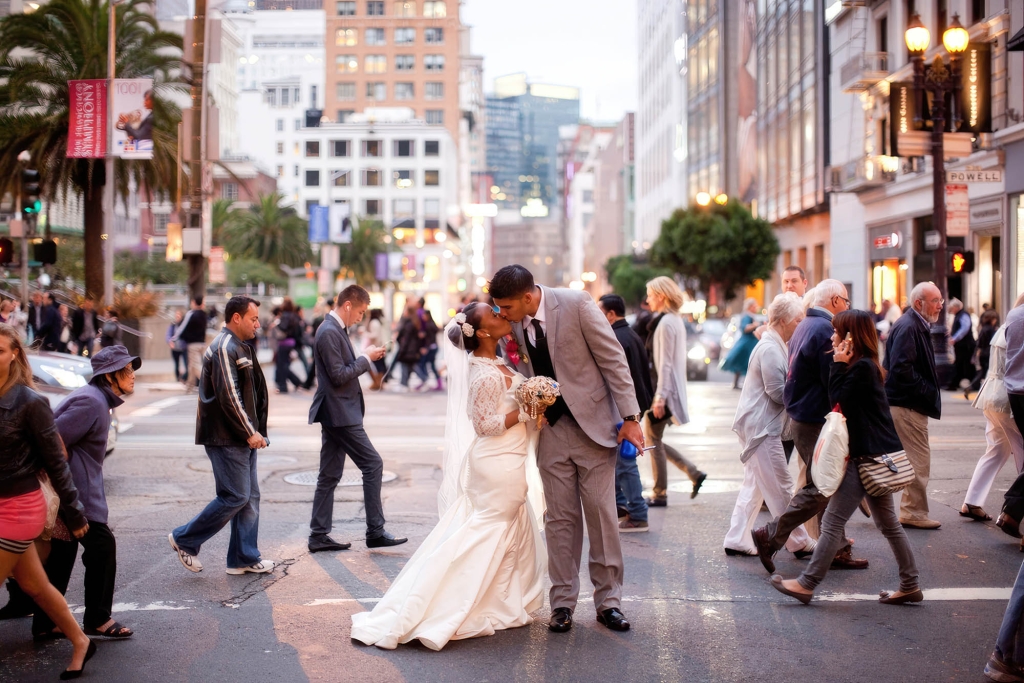 A bride and groom standing in the busy streets of san francisco sharing a kiss